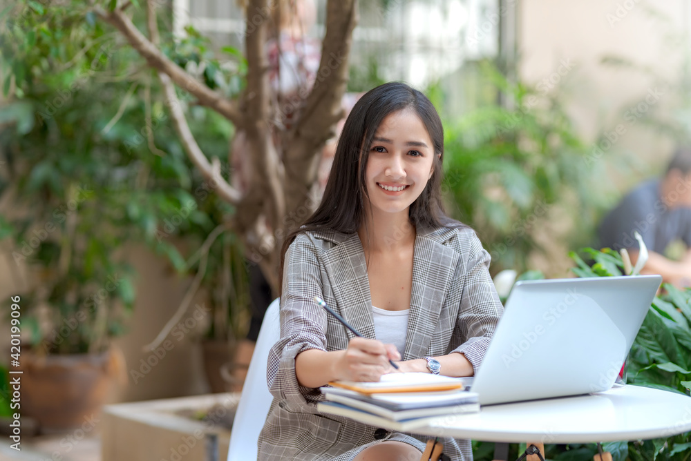 Beautiful Asian woman sitting  taking notes at a coffee shop. Looking at camera.