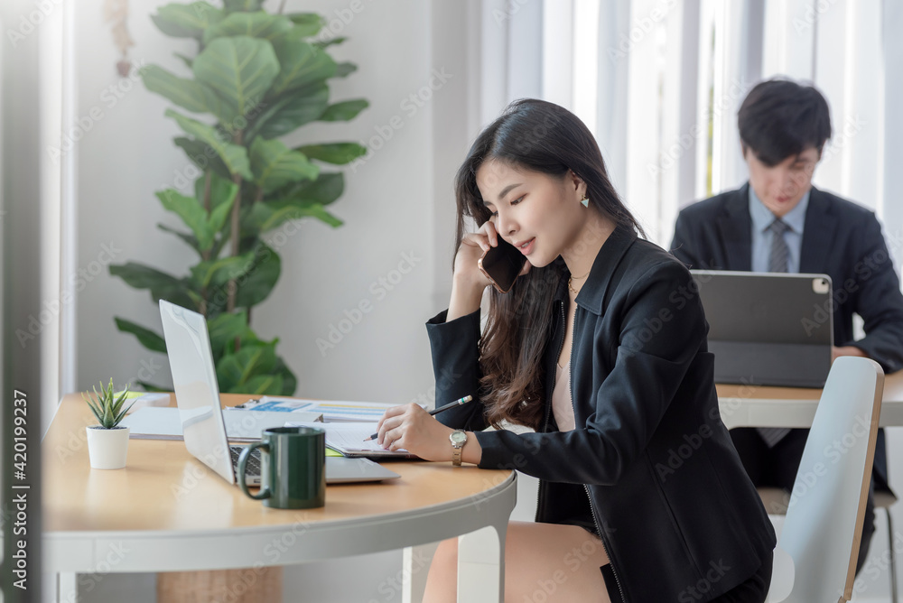 Young businesswoman talking on mobile phone taking notes in modern office. Young businesswoman talking on mobile phone taking notes in modern office.