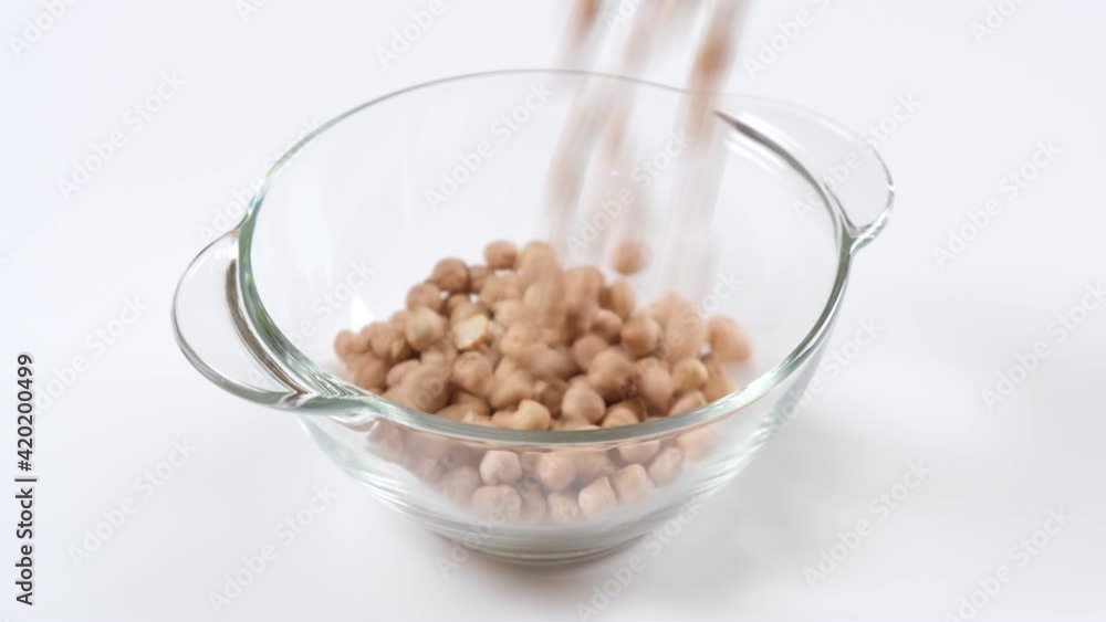 Dry raw chickpeas falling into a glass bowl on white background, slow motion Dry raw chickpeas falling into a glass bowl on white background, slow motion