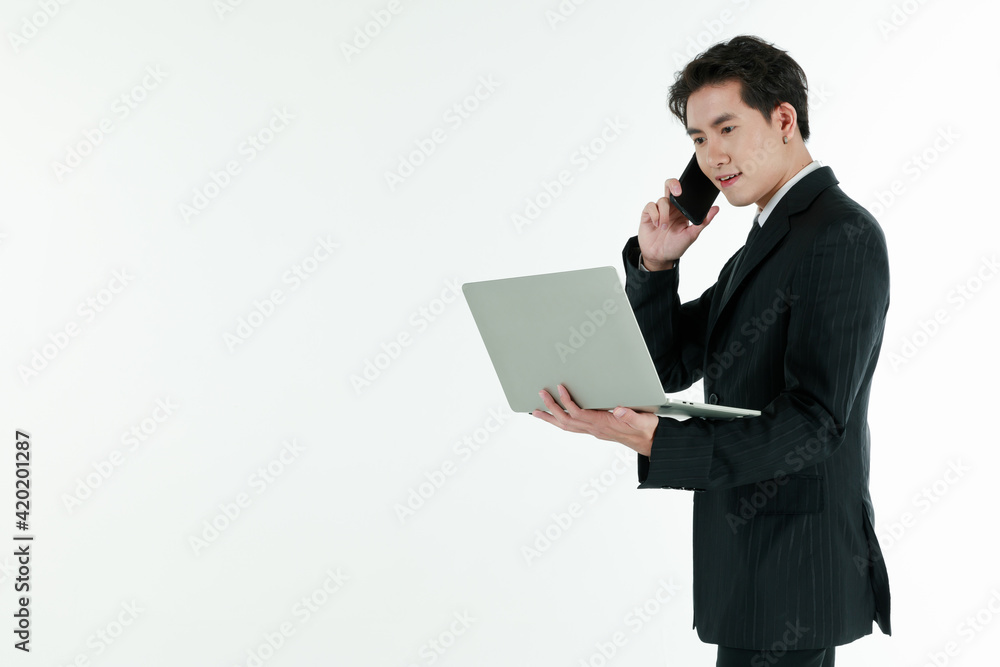 Portrait of self confidence young and handsome business Asian man in black suit holding notebook laptop computer and talking on smartphone with copy space studio shot isolated on white background Portrait of self confidence young and handsome business Asian man in black suit holding notebook laptop computer and talking on smartphone with copy space studio shot isolated on white background