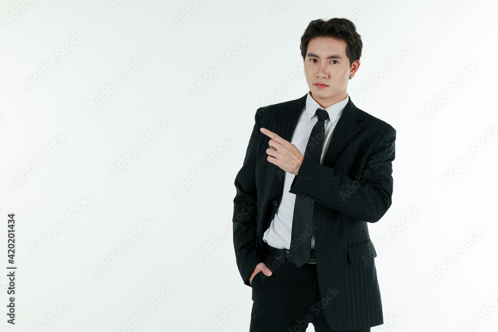 Portrait of self-confidence young and handsome Asian businessman in black suit standing in elegant pose and pointing finger, copy space studio shot isolated on white background Portrait of self-confidence young and handsome Asian businessman in black suit standing in elegant pose and pointing finger, copy space studio shot isolated on white background