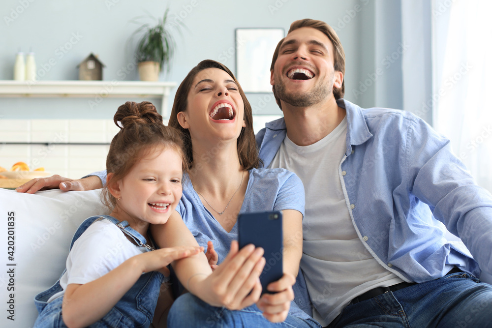 Beautiful young family with little child taking a selfie with a smartphone at home on the couch.