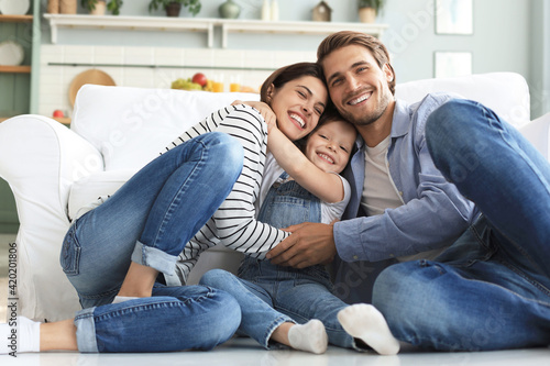 Young Caucasian family with small daughter pose relax on floor in living room, smiling little girl kid hug embrace parents, show love and gratitude, rest at home together. photo