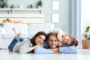 Young Caucasian family with small daughter pose relax on floor in living room, smiling little girl kid hug embrace parents, show love and gratitude, rest at home together.