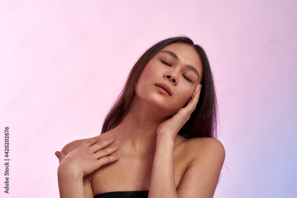 Looking and feeling gorgeous. Young sensual asian woman keeping eyes closed, touching her healthy soft face skin while standing against pink background Looking and feeling gorgeous. Young sensual asian woman keeping eyes closed, touching her healthy soft face skin while standing against pink background