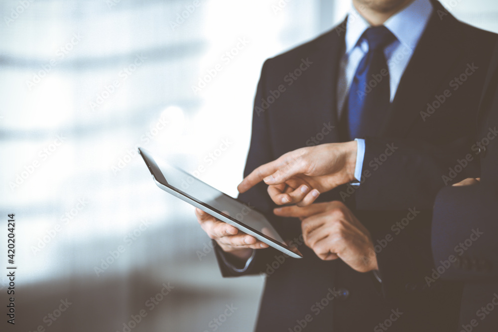 Business people use a tablet computer for discussion of their new project, standing in a modern office. Unknown businessman or male entrepreneur with a colleague at workplace. Teamwork and partnership Business people use a tablet computer for discussion of their new project, standing in a modern office. Unknown businessman or male entrepreneur with a colleague at workplace. Teamwork and partnership