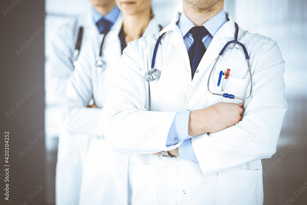 Group of modern doctors standing as a team with crossed arms and stethoscopes in hospital office. Physicians ready to examine and help patients. Medical help, insurance in health care, best desease Group of modern doctors standing as a team with crossed arms and stethoscopes in hospital office. Physicians ready to examine and help patients. Medical help, insurance in health care, best desease