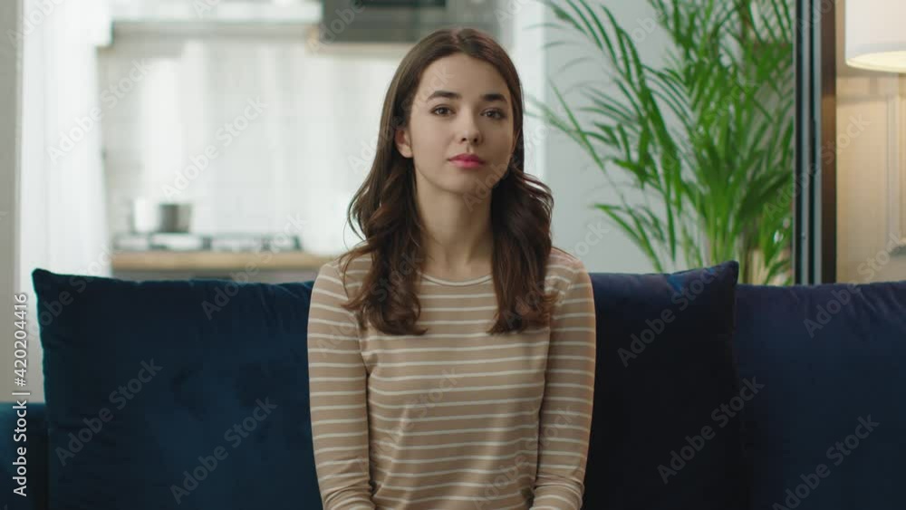 Confident smiling young adult european woman looking at camera sitting on sofa at home office. Confident smiling young adult european woman looking at camera sitting on sofa at home office.