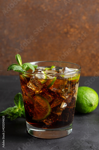 cuba libre, rum and cola cocktail in glass with a lime and mint on black background