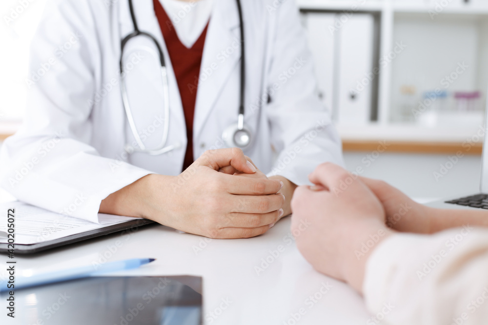 Unknown woman-doctor and patient discussing something while sitting at the table in clinic, close-up. Medicine concept Unknown woman-doctor and patient discussing something while sitting at the table in clinic, close-up. Medicine concept