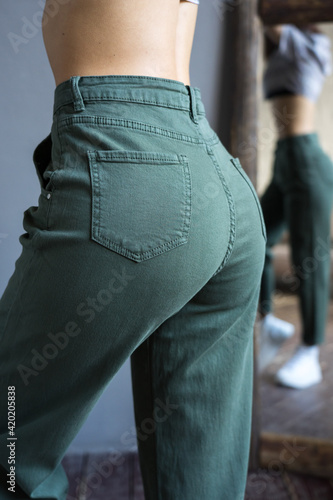  young cute girl posing in a room in green jeans against a mirror