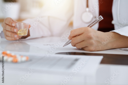 Unknown woman-doctor fills up prescription form in sunny room, close-up