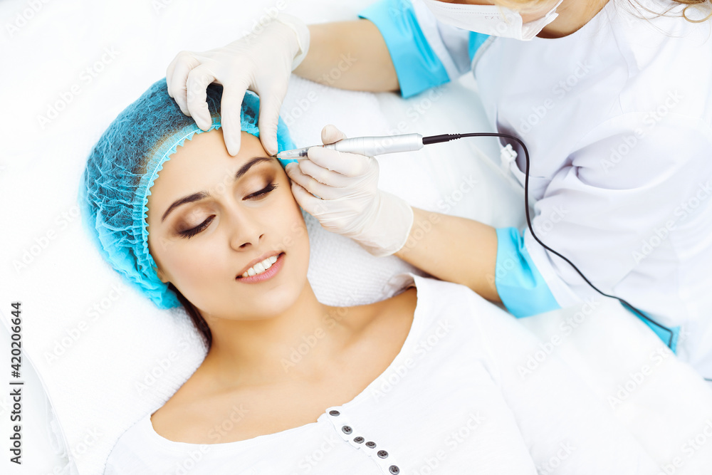 Naklejka premium Professional beautician doing eyebrow tattoo at woman face. Permanent brow makeup in beauty salon, closeup. Cosmetology treatment