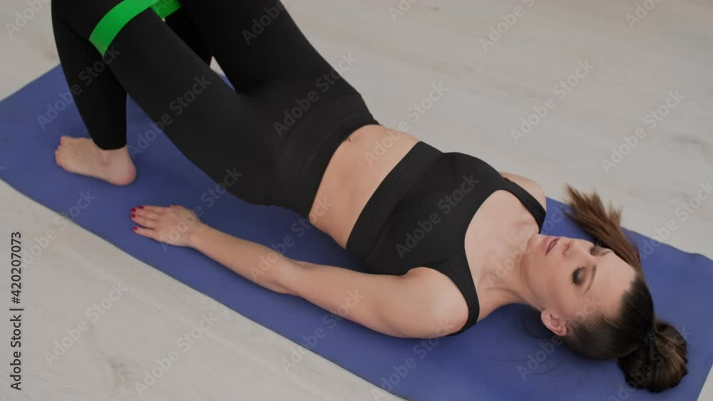 Concentrated sporty woman training and performing physical exercises with elastic band indoors. Young female in sportswear working out at home. Home fitness concept. Lockdown. 4K, UHD Concentrated sporty woman training and performing physical exercises with elastic band indoors. Young female in sportswear working out at home. Home fitness concept. Lockdown. 4K, UHD