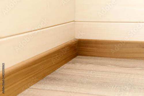 A corner of the room with wood-paneled walls, wooden skirting boards and a wooden floor