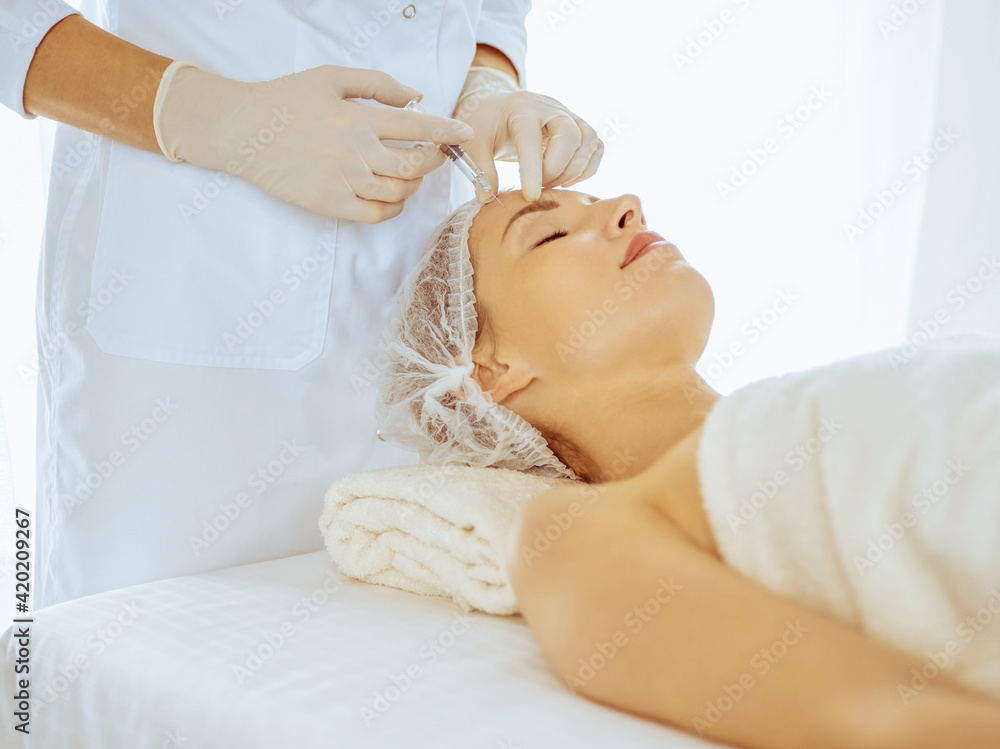 Beautiful woman receiving beauty injections with closed eyes in medical center. Beautician doctor hands doing beauty procedure to female face with syringe
