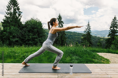 Young fit woman stretching or doing squats on yoga mat at sunny mountains. Outdoor workout, training