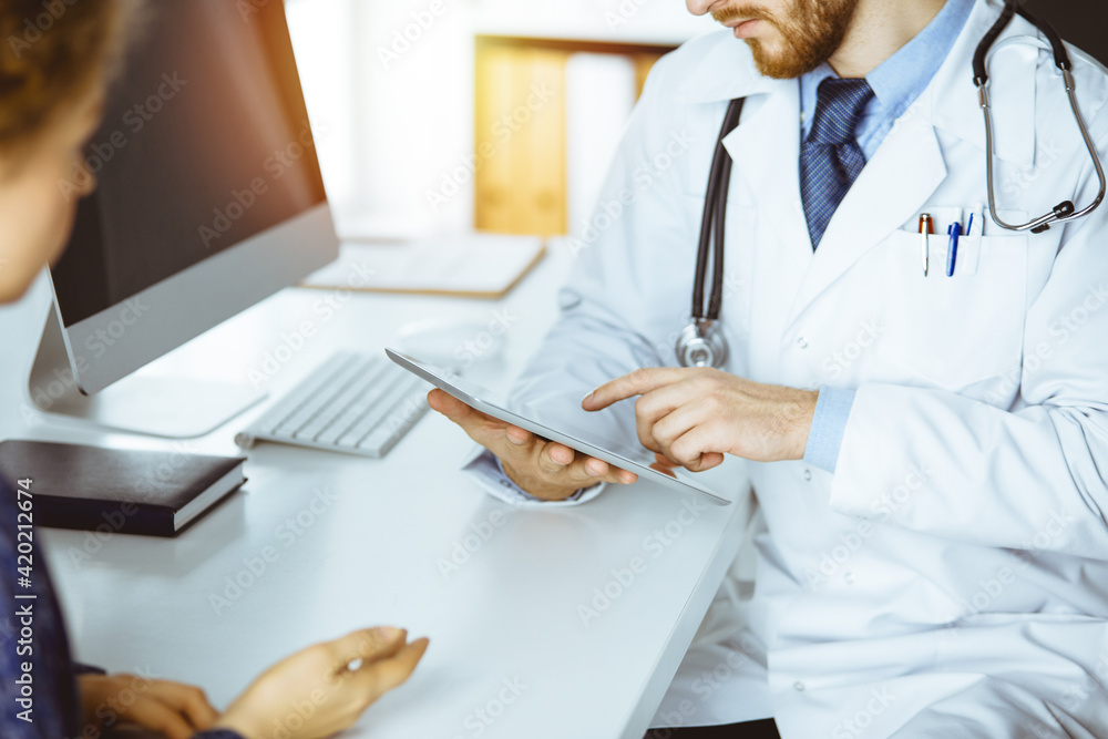 Friendly male doctor and patient woman discussing current health examination while sitting in sunny clinic Friendly male doctor and patient woman discussing current health examination while sitting in sunny clinic