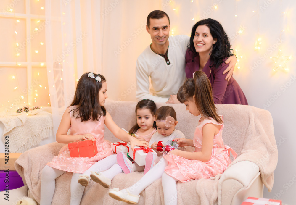 family portrait of a parents and children, sitting on a couch in home interior decorated with lights and gifts