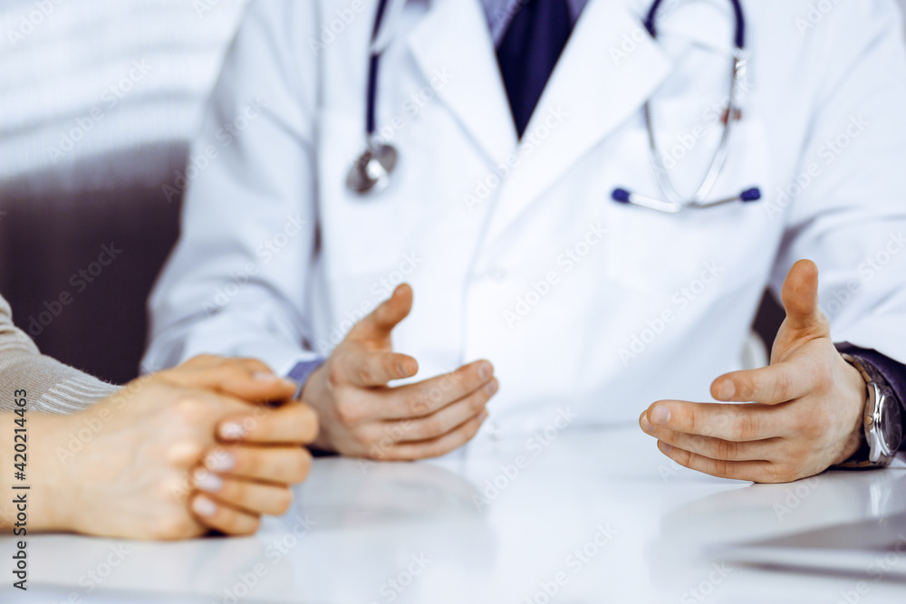 Unknown male doctor and patient woman discussing something while sitting in clinic. Best medical service in hospital, medicine, pandemic stop Unknown male doctor and patient woman discussing something while sitting in clinic. Best medical service in hospital, medicine, pandemic stop