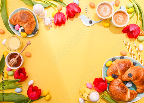 Spring Easter breakfast. Two Espresso coffee in bright cups  Easter chocolate eggs  pink bunny ears and red tulips on a yellow background. Above. Copy space. Flat lay