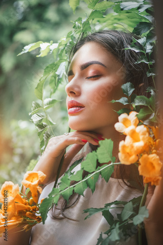 Beautiful young woman posing in Trumpet vine flowers in summer garden. Beauty model girl with Campsis. Enjoying nature outdoor. 