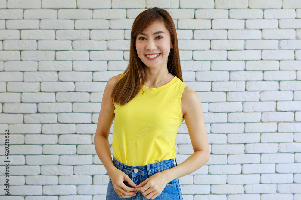 Portrait of young and beautiful brunette dark hair Asian woman in yellow Sleeveless shirt pose with smile and happy friendly face on white brick wall background. Portrait of young and beautiful brunette dark hair Asian woman in yellow Sleeveless shirt pose with smile and happy friendly face on white brick wall background.
