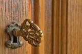 Stary klucz włożony do zamka dębowej szafy.