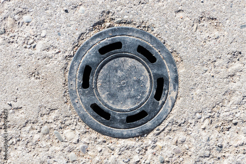 Round manhole on concrete drain system cover. Urban sewer background. Metal drain cover texture. Empty copy space industrial background. 