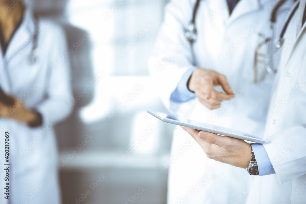 Group of unknown doctors use a computer tablet to check up some medical names records, while standing in a hospital office. Physicians ready to examine and help patients. Medical help, insurance in Group of unknown doctors use a computer tablet to check up some medical names records, while standing in a hospital office. Physicians ready to examine and help patients. Medical help, insurance in