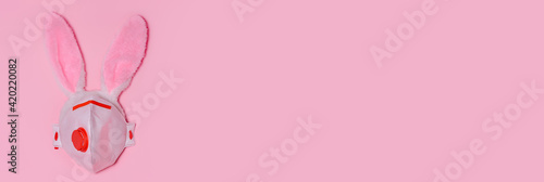 Pink bunny rabbit with face protective mask on pink background. Easter quarantine concept.Copy space for text, top view, flat lay. Banner © syhin_stas