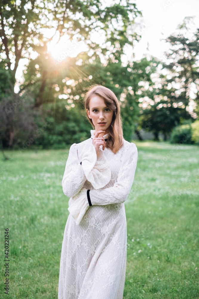 Portrait of beautiful caucasian woman in long white retro dress walking in green summer blossom park on meadow. Rays of sunlight. Lady girl. Book cover Portrait of beautiful caucasian woman in long white retro dress walking in green summer blossom park on meadow. Rays of sunlight. Lady girl. Book cover