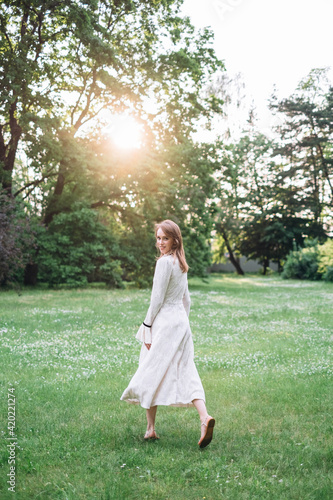 Portrait of beautiful caucasian woman in long white retro dress walking in green summer blossom park on meadow. Rays of sunlight. Lady girl. Book cover © alex