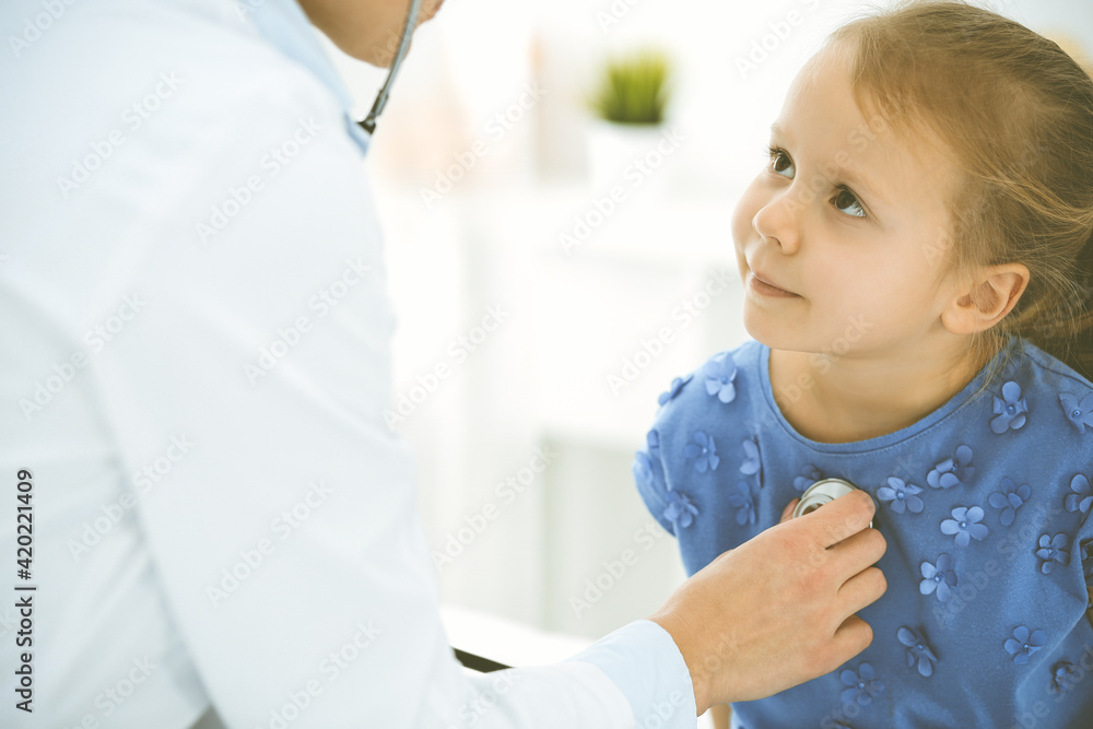 Doctor examining a child by stethoscope. Happy smiling girl patient dressed in blue dress is at usual medical inspection. Medicine concept Doctor examining a child by stethoscope. Happy smiling girl patient dressed in blue dress is at usual medical inspection. Medicine concept