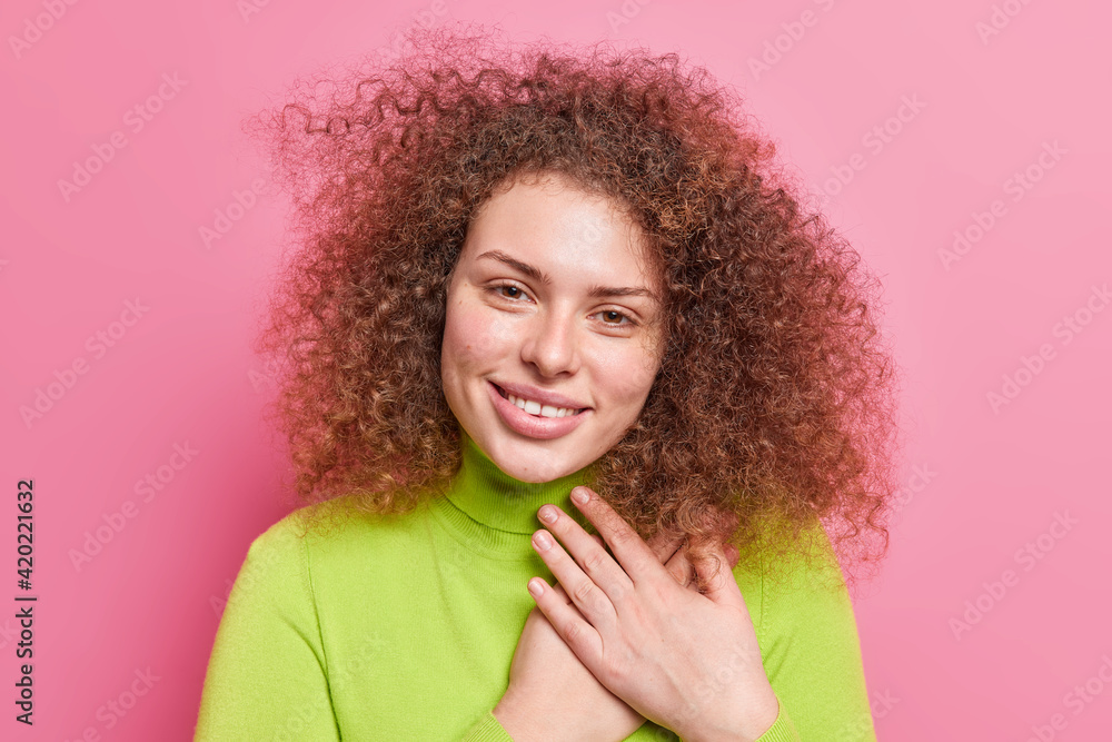 Thank you very much. Smiling good looking woman with curly hair holds hands on chest expresses gratutude and appreciation being touched dressed in green poloneck isolated over pink background Thank you very much. Smiling good looking woman with curly hair holds hands on chest expresses gratutude and appreciation being touched dressed in green poloneck isolated over pink background