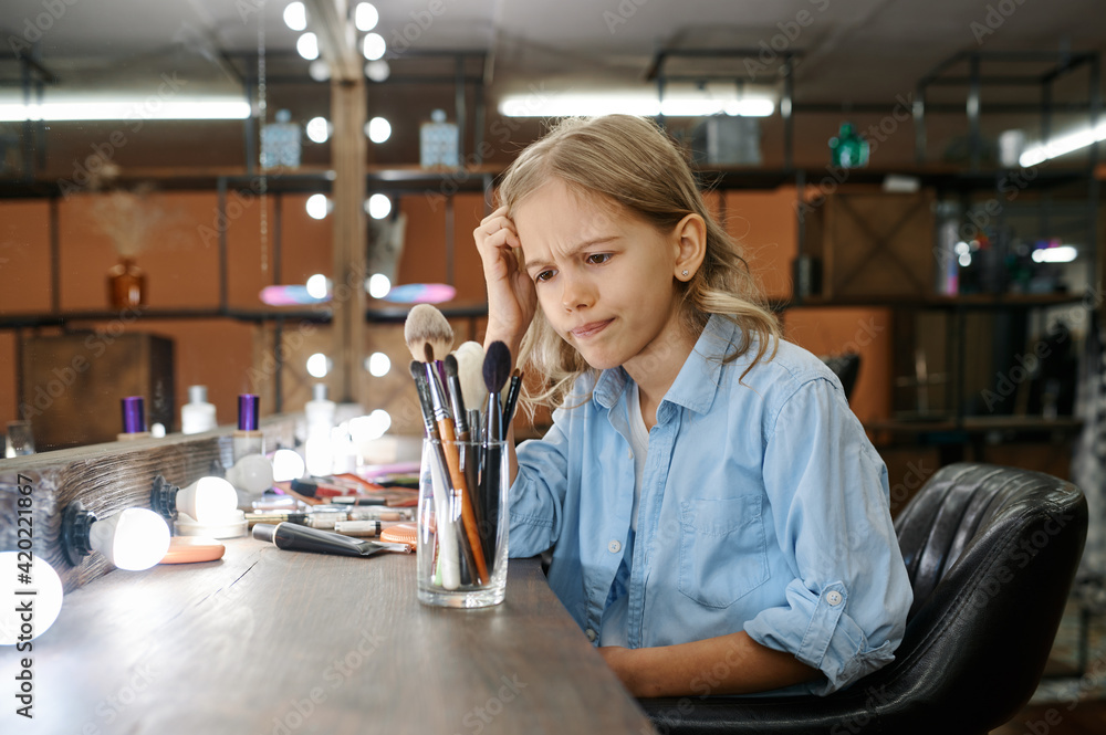 Serious little girl looks on cosmetics, makeup Serious little girl looks on cosmetics, makeup