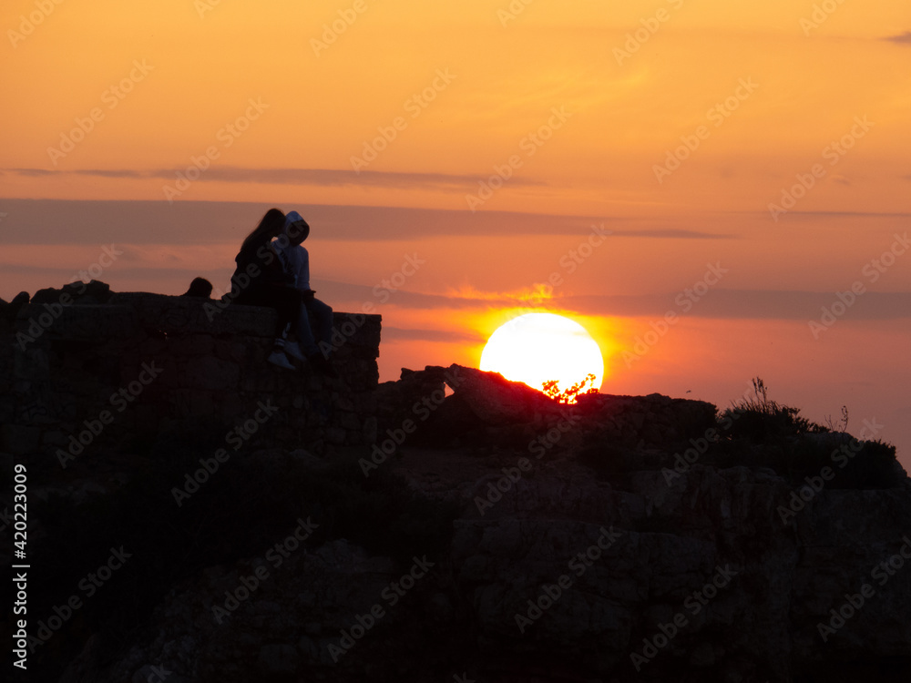Couple's silhouette on a rock looking the sunset