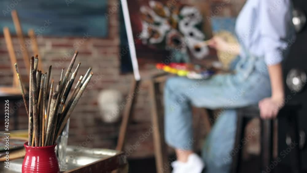 Young beautiful female artist painting still life with sunflower on canvas using oil paintings and art brush. Woman student at fine art course. Relaxation, leisure, hobby, stress management.