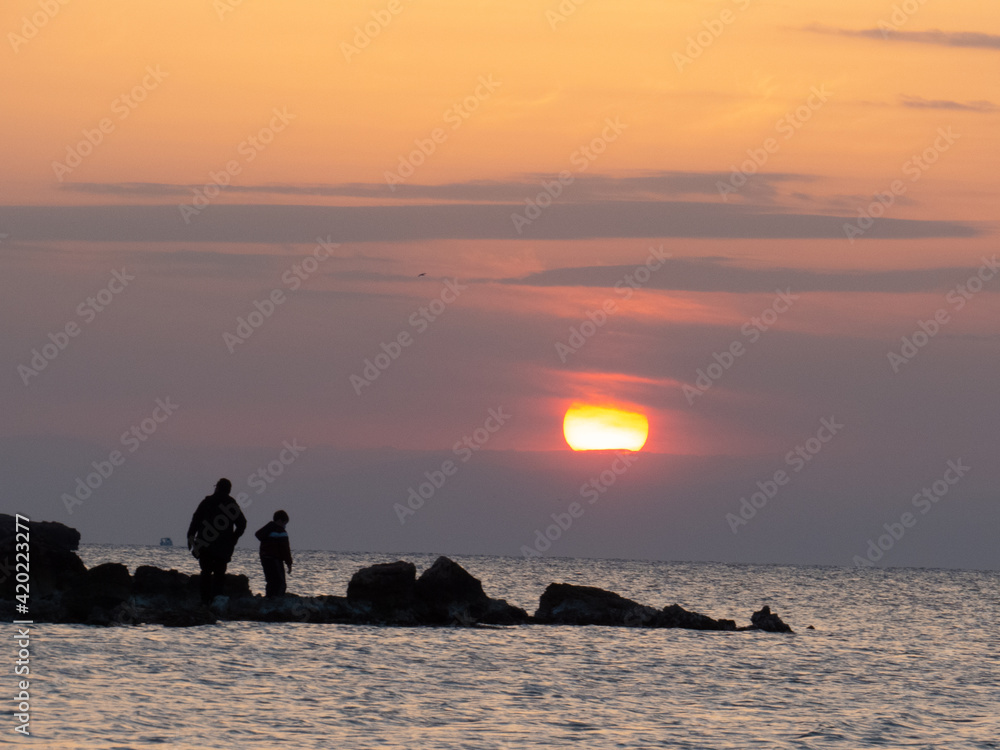Father's and boy's silhouette on a rock looking the sunset