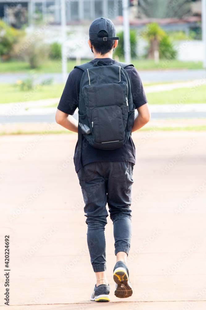 Person in back cap walking in black clothes and with backpack on his back Person in back cap walking in black clothes and with backpack on his back