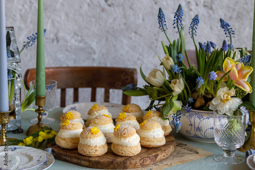 Choux Buns with Craquelin (crispy cream puffs) filled cream on a table decorated with spring flowers