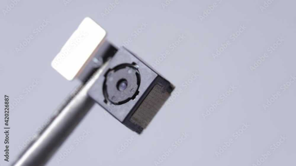 Close-up on the mobile phone camera module. Close-up tweezers or clip holds smartphone lens in studio shot white white background Close-up on the mobile phone camera module. Close-up tweezers or clip holds smartphone lens in studio shot white white background