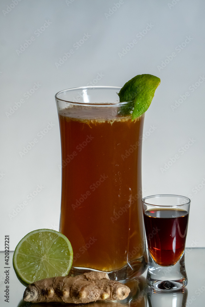 Brown herbal alcohol drink with ginger beer and fresh grated ginger. Lemon zest on the top of a glass. Single shot and ginger around. Reflection on the bottom and gradient background Brown herbal alcohol drink with ginger beer and fresh grated ginger. Lemon zest on the top of a glass. Single shot and ginger around. Reflection on the bottom and gradient background