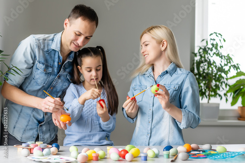 Mother, father and daughter are painting eggs. Happy family are preparing for Easter.