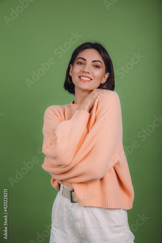 Young woman in casual peach sweater isolated on green olive color background love concept, holding hands crossed hugging herself