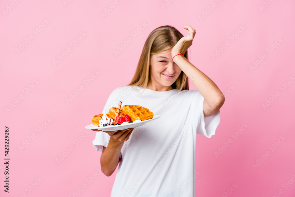 Young russian woman eating a waffle isolated forgetting something, slapping forehead with palm and closing eyes.