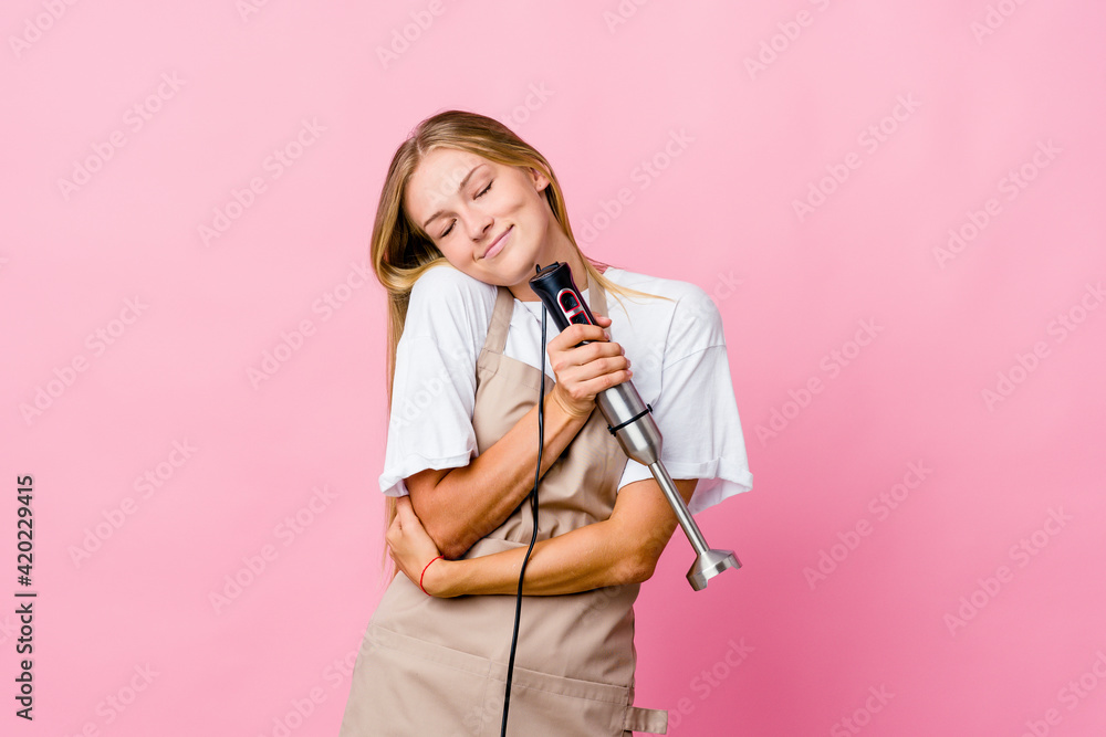 Young russian cook woman holding an electric mixer isolated hugs, smiling carefree and happy. Young russian cook woman holding an electric mixer isolated hugs, smiling carefree and happy.