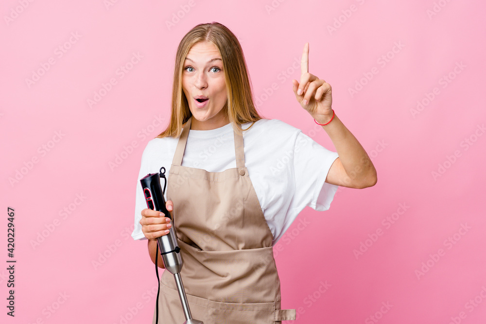 Young russian cook woman holding an electric mixer isolated having an idea, inspiration concept. Young russian cook woman holding an electric mixer isolated having an idea, inspiration concept.