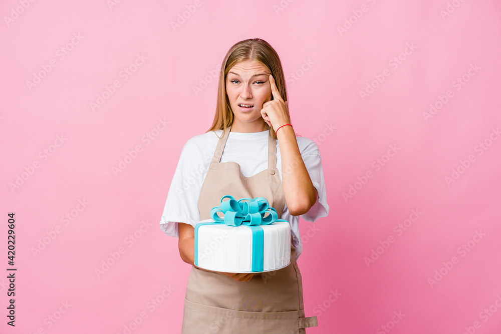 Young russian baker woman holding a delicious cake showing a disappointment gesture with forefinger. Young russian baker woman holding a delicious cake showing a disappointment gesture with forefinger.