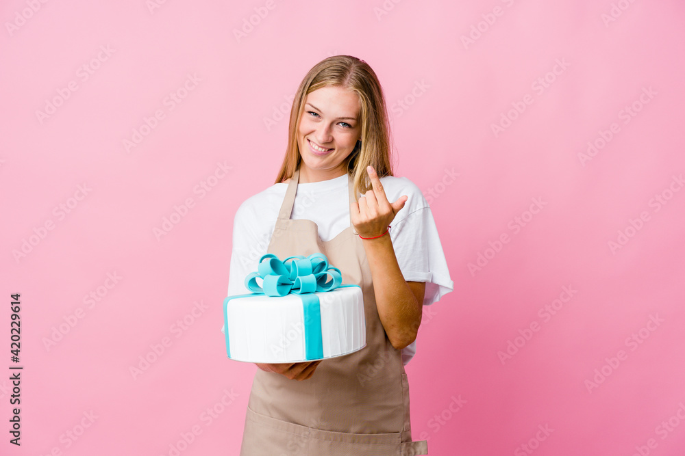 Young russian baker woman holding a delicious cake pointing with finger at you as if inviting come closer. Young russian baker woman holding a delicious cake pointing with finger at you as if inviting come closer.